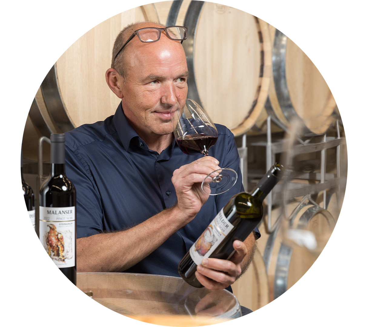 Un collaborateur examine attentivement les arômes d’un vin rouge. Des fûts en bois sont visibles à l’arrière-plan.