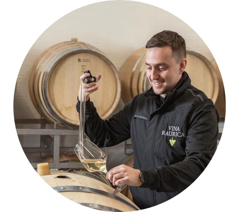 Un collaboratore controlla un vino in cantina, tra le botti.
