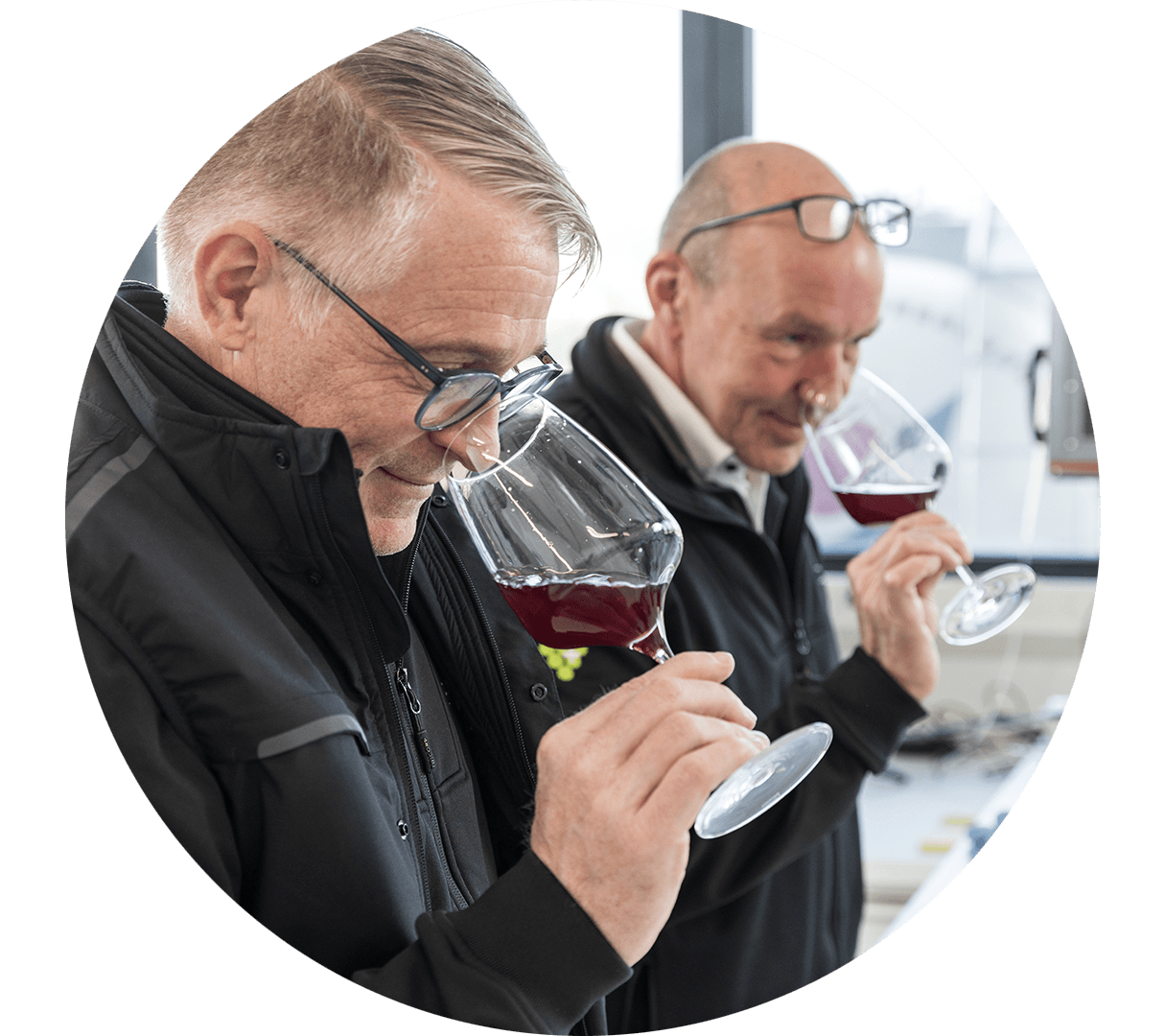 Nel laboratorio, due collaboratori annusano un calice di vino rosso.